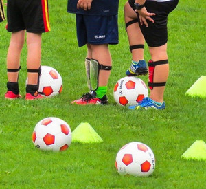 Kinderfüße auf einem Rasenplatz, Fußbälle liegen im Vordergrund