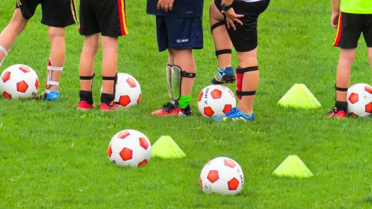 Kinderfüße auf einem Rasenplatz, Fußbälle liegen im Vordergrund